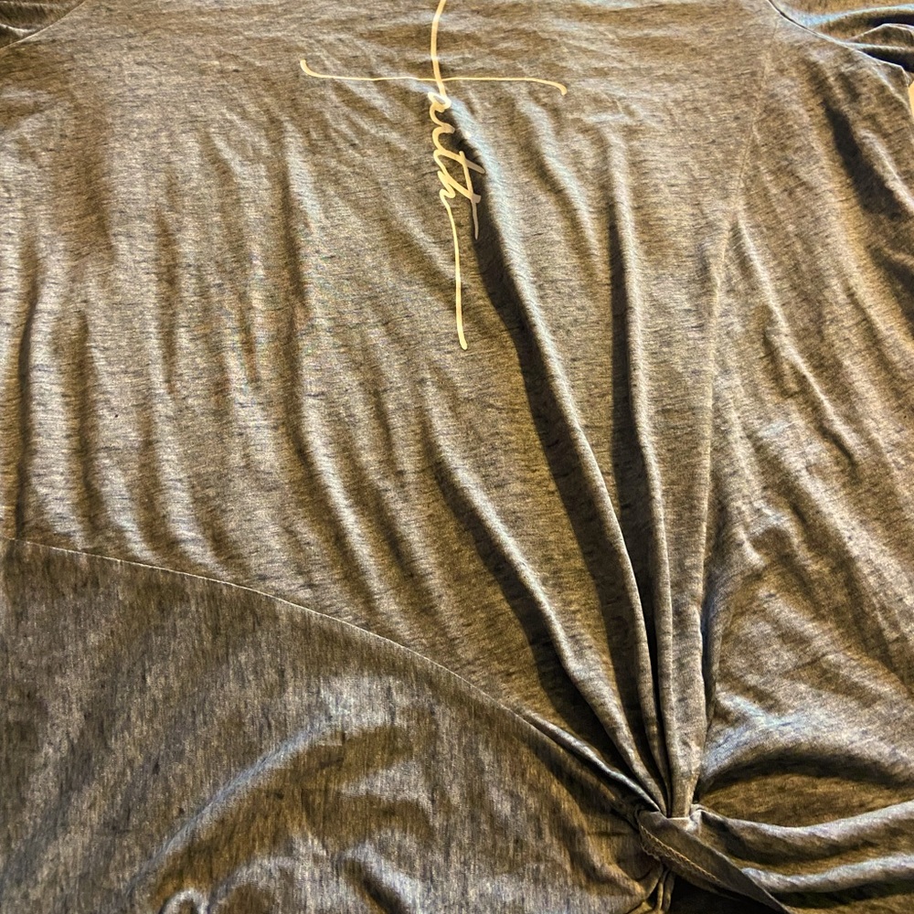 Grey shirt, says “faith” in the middle, decorated knot on the bottom…